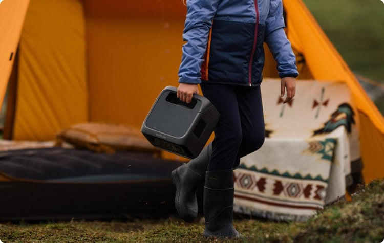 Pessoa carregando uma estação de energia portátil EcoFlow em um acampamento ao ar livre, destacando sua portabilidade e praticidade para aventuras na natureza